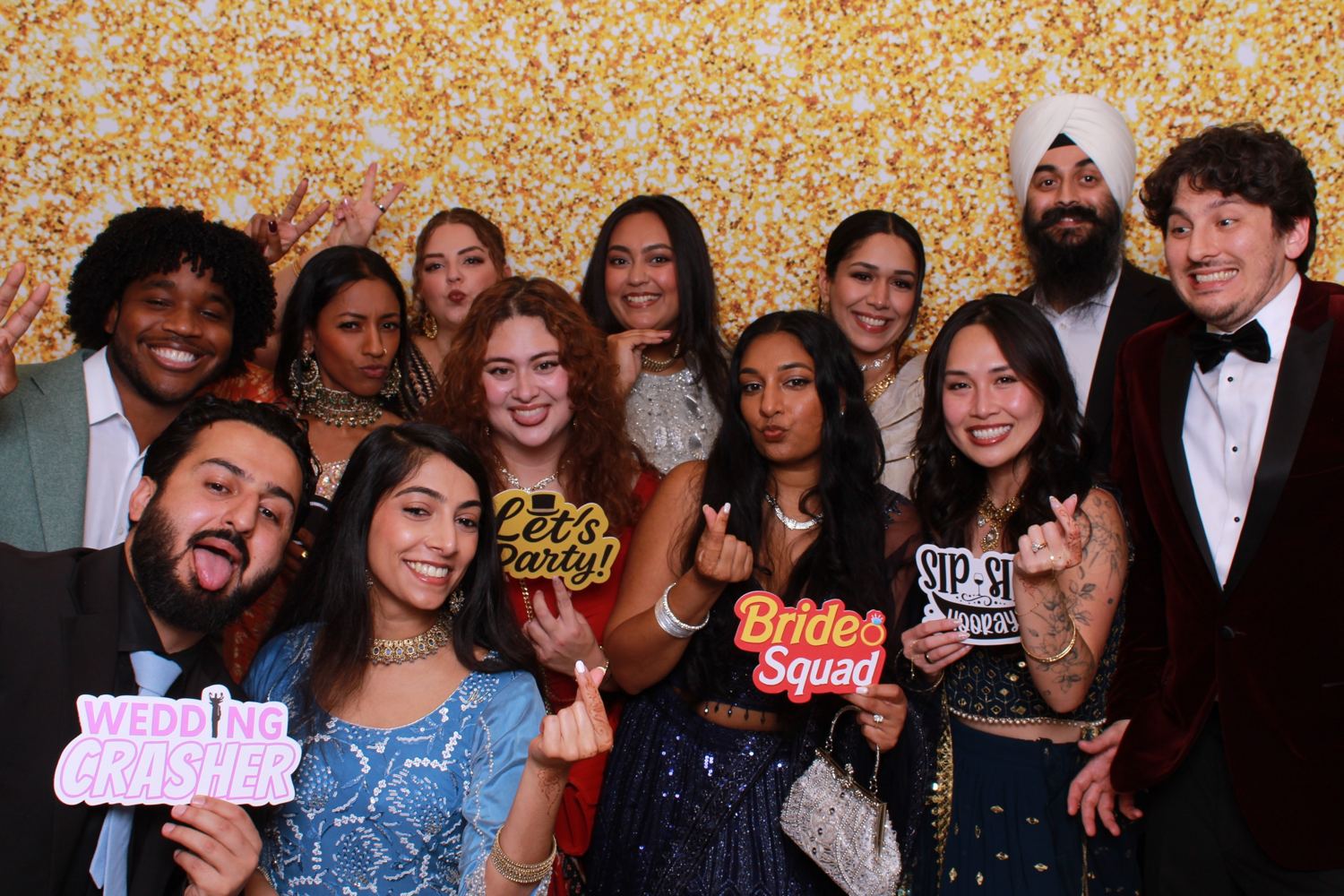 Ten guests in formal wear laughing with props in front of a gold glitter backdrop