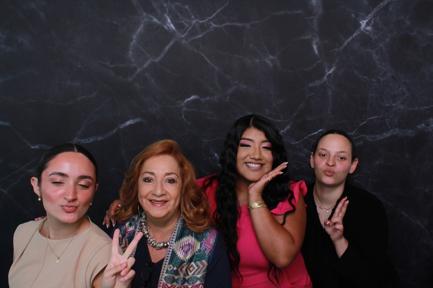 Four women posing together in front of a black marble backdrop