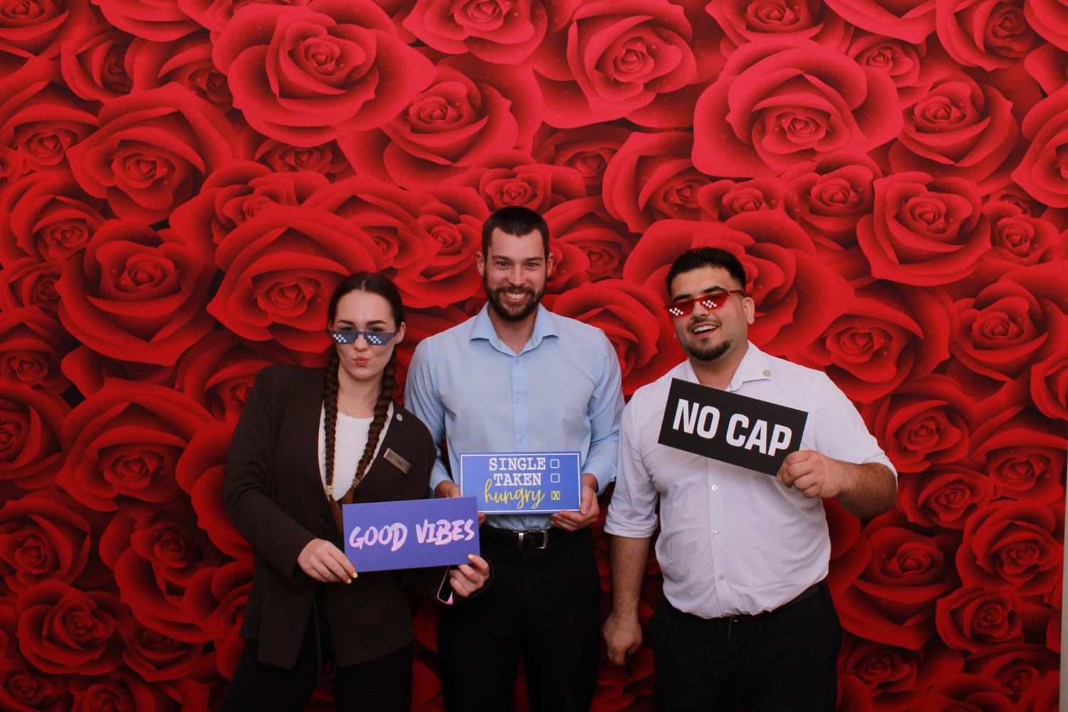 Three coworkers holding props in front of a red roses backdrop