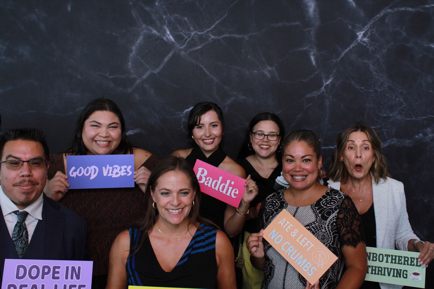 Seven colleagues holding colorful signs in front of a black marble backdrop