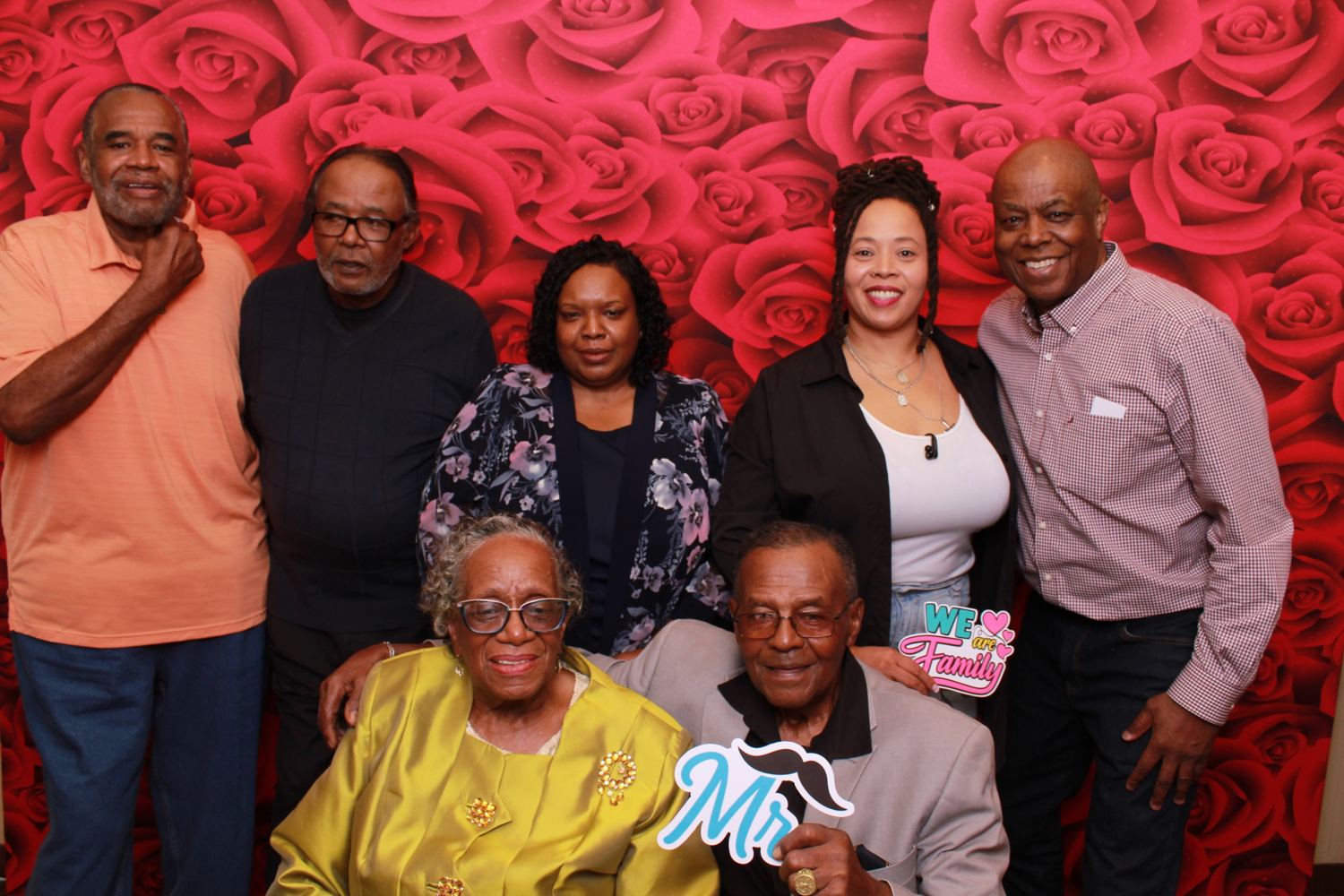 A multi-generation family portrait in front of a red roses backdrop