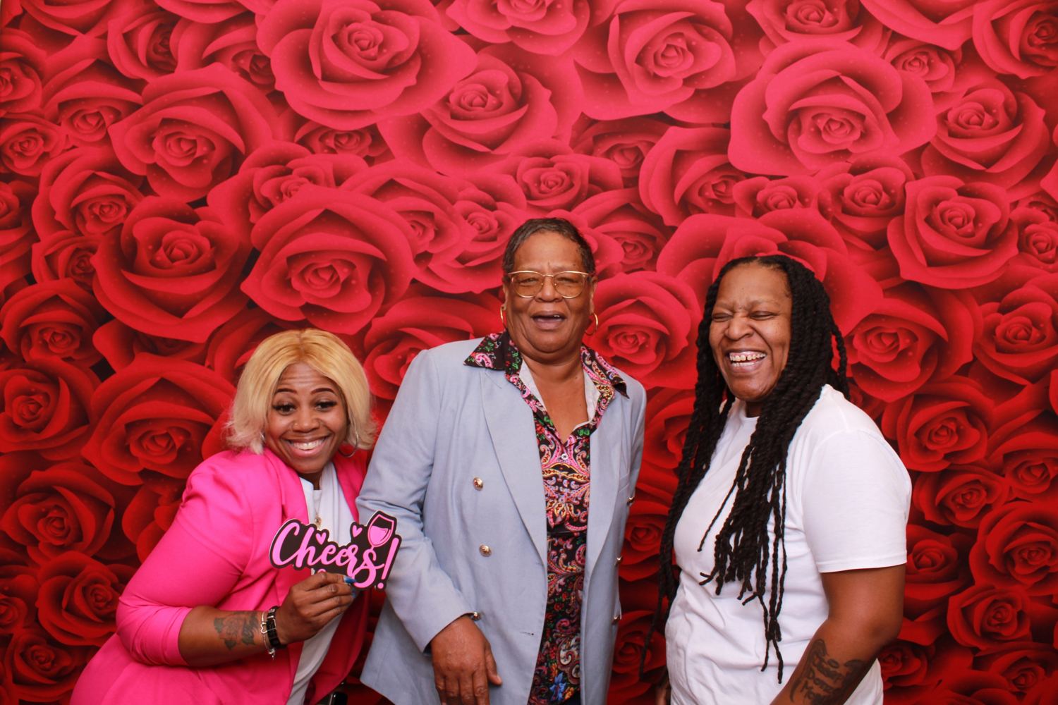 Three women laughing in front of a red roses backdrop