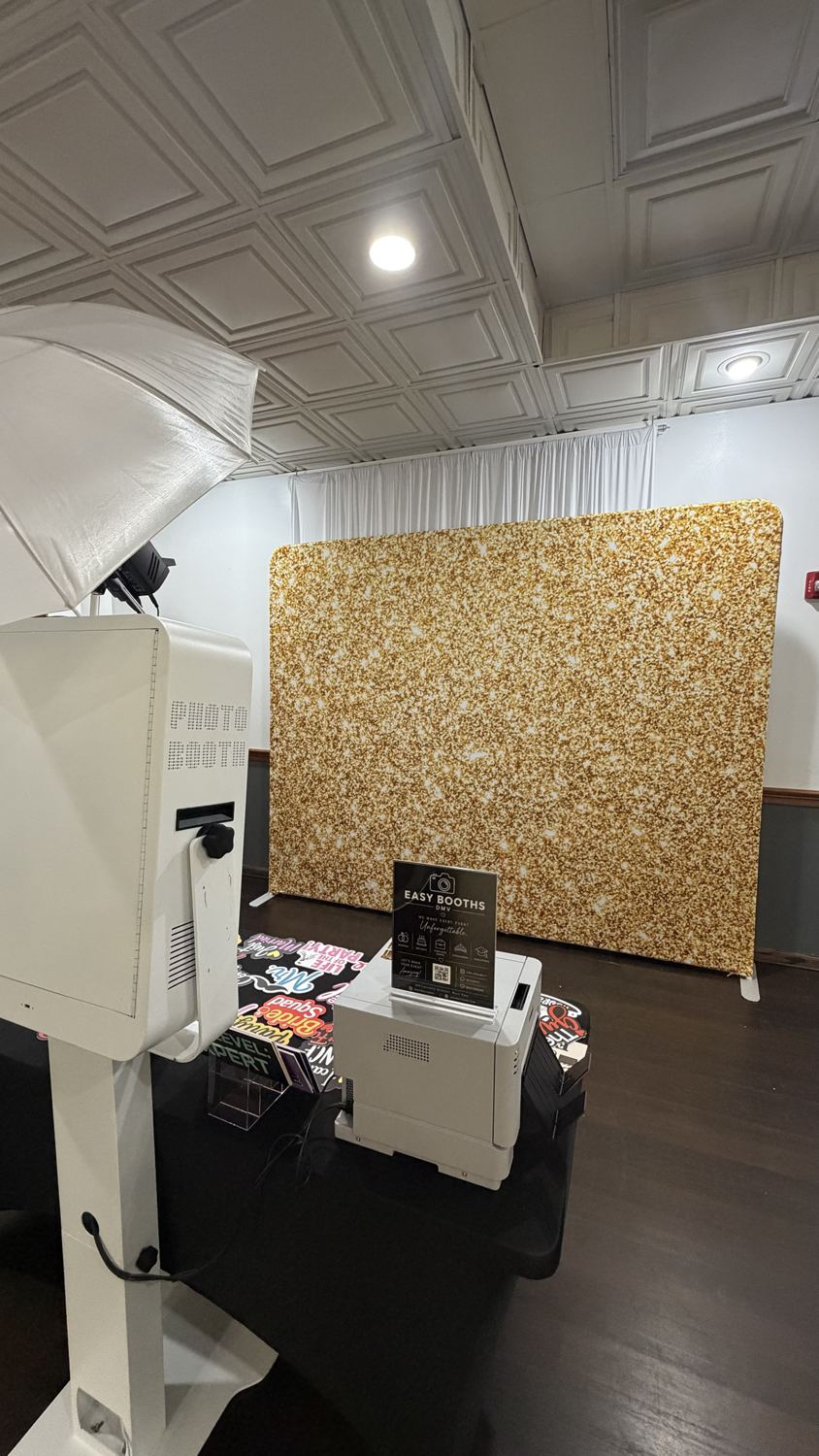 Photo booth and printer facing a gold glitter backdrop in a banquet hall