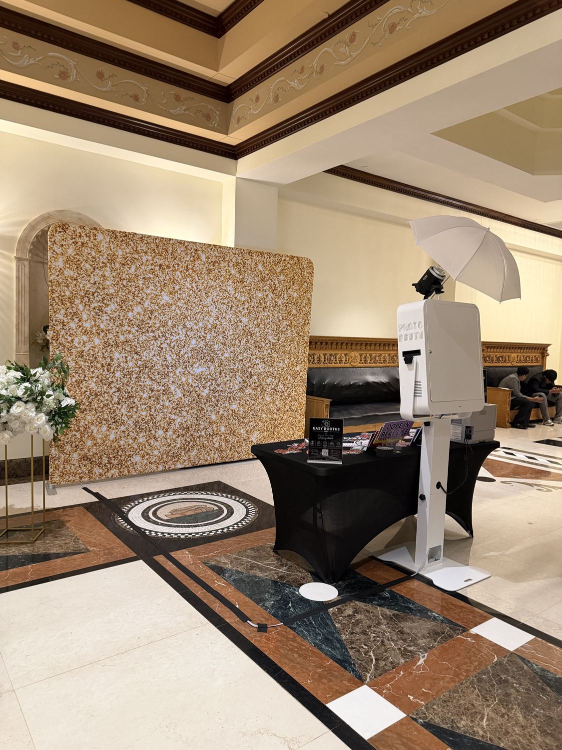 Photo booth and gold glitter backdrop in an ornate hall with marble floors