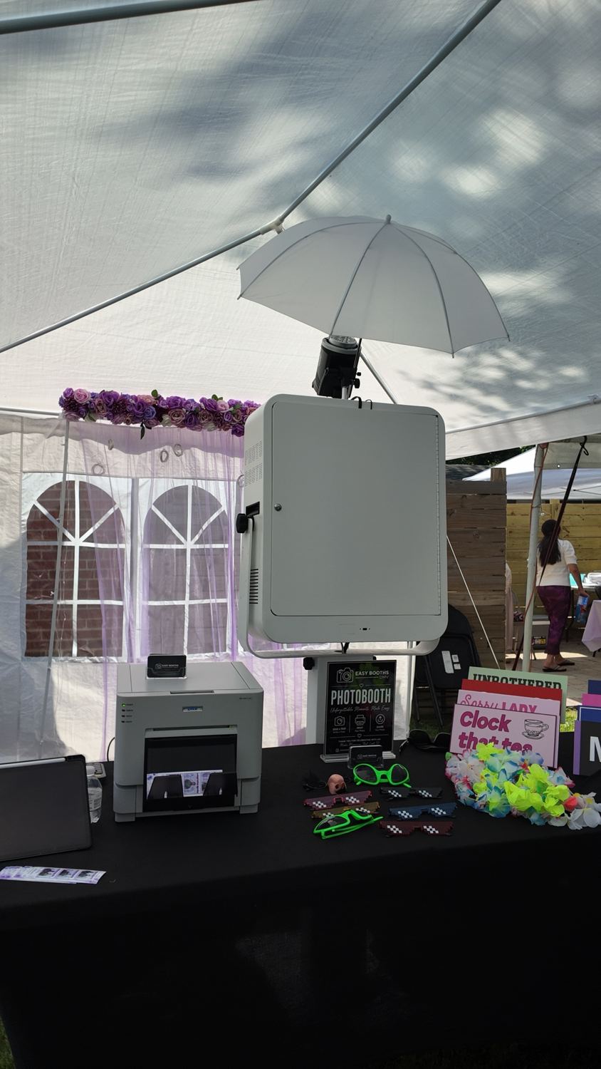 Photo booth, printer and props under a white party tent with a purple flower arch